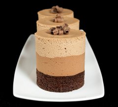 A photo of 3 Triple Chocolate Mousse Cakes displayed in a row on a white rectangular dish with a black background.