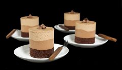 A photo of 4 Chocolate Mousse Cakes layered with Dark Chocolate Cake, Bittersweet Chocolate Mousse and Milk Chocolate Mousse displayed on small white dessert dishes with dessert forks with a black background.