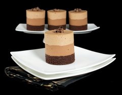 A photo of 4 Triple Chocolate Mousse Cakes, one placed in front on a white dessert plate and 3 in the background on a white cake stand.