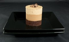 A photo of gourmet cake, Chocolate Mousse Cake with chocolate curls on a black dessert dish.